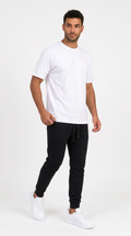 A man modeling a white crew-neck t-shirt and black jogger pants with white sneakers, standing against a plain white studio background, from Meleche Fashion USA or Meléche (short as (Mé))