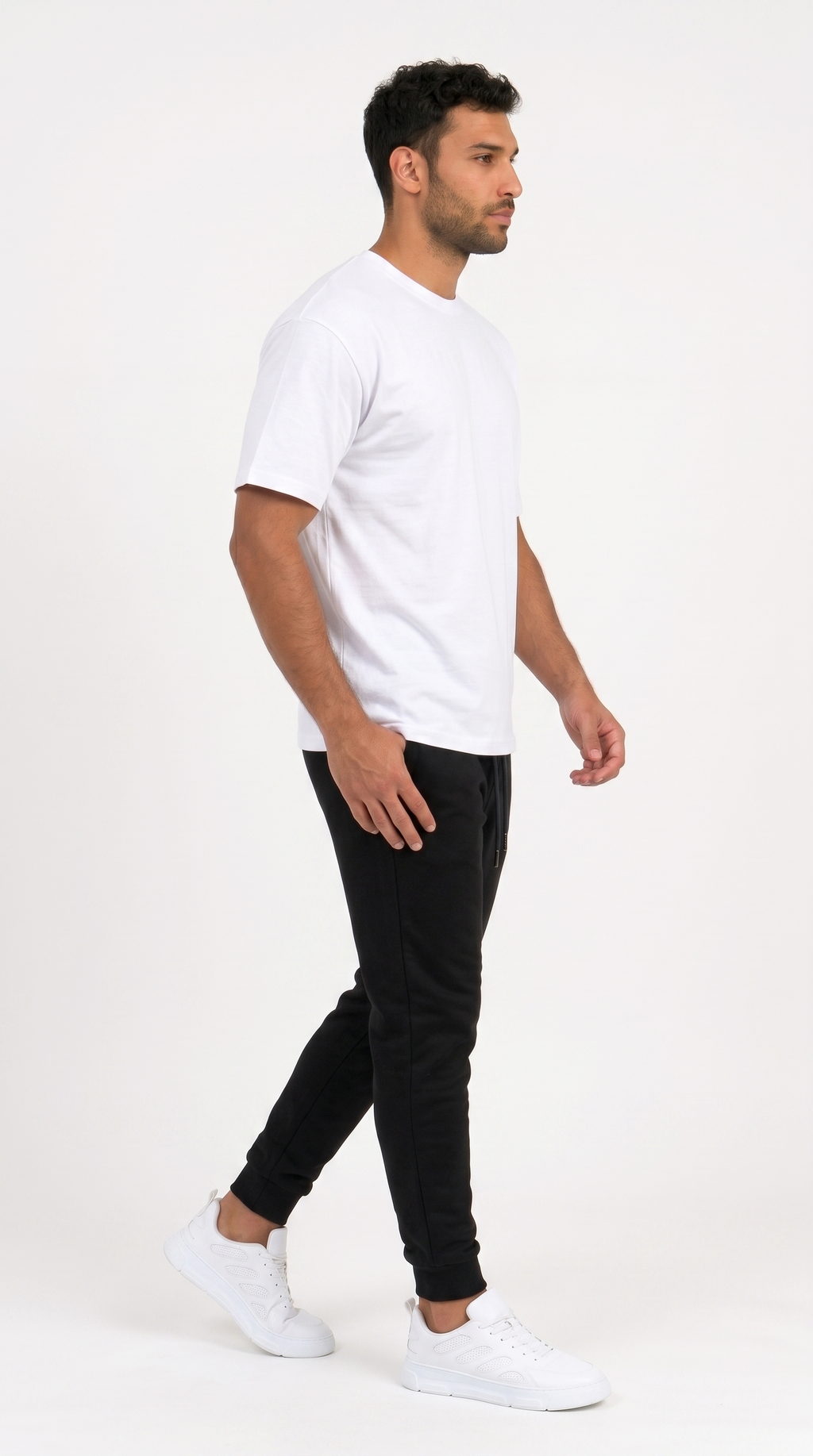 A man in profile wearing a plain white short-sleeve crewneck t-shirt, black jogger pants, and white sneakers, standing against a solid white studio background, from Meleche Fashion USA or Meléche (short as (Mé))