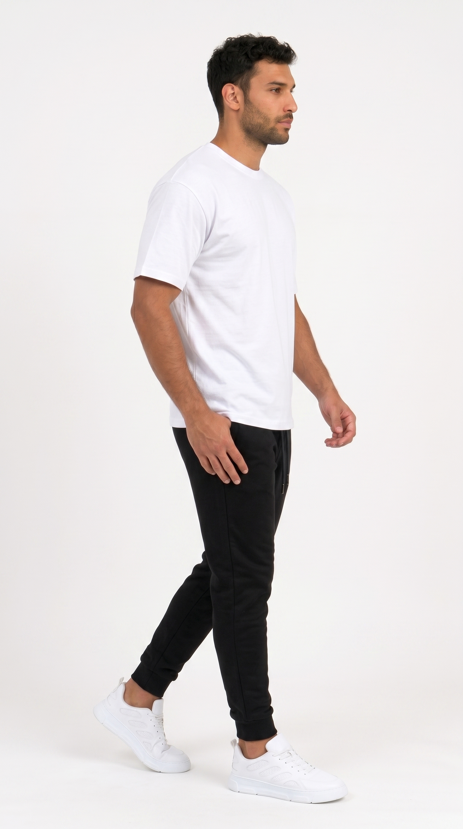 A man in profile wearing a plain white short-sleeve crewneck t-shirt, black jogger pants, and white sneakers, standing against a solid white studio background, from Meleche Fashion USA or Meléche (short as (Mé))