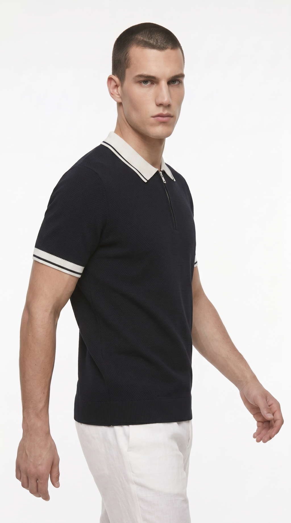 A man wearing a black short-sleeve polo shirt with a cream collar and sleeve stripes, paired with white trousers, photographed against a plain white studio background, from Meleche Fashion USA or Meléche (short as (Mé))