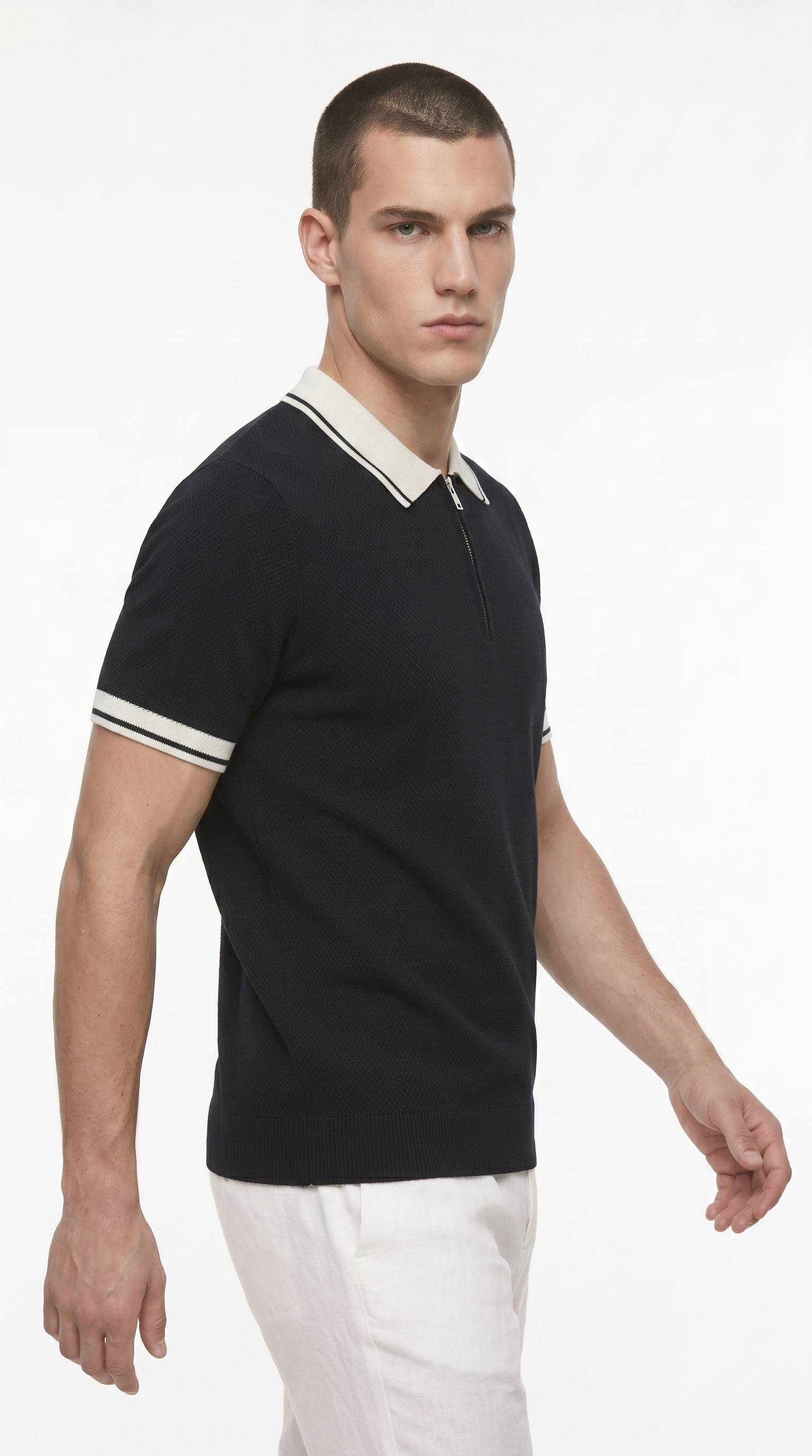 A man wearing a black short-sleeve polo shirt with a cream collar and sleeve stripes, paired with white trousers, photographed against a plain white studio background, from Meleche Fashion USA or Meléche (short as (Mé))