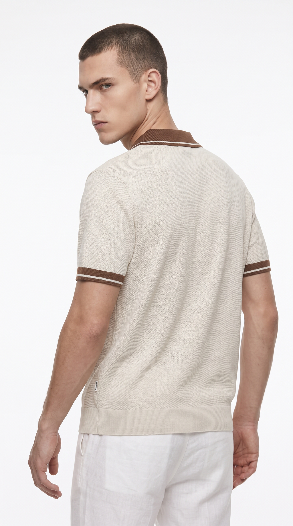 A man wearing a cream-colored short-sleeve knit polo shirt with brown trim on the collar and sleeve cuffs, shown from a three-quarters back view against a plain white studio background, from Meleche Fashion USA or Meléche (short as (Mé))