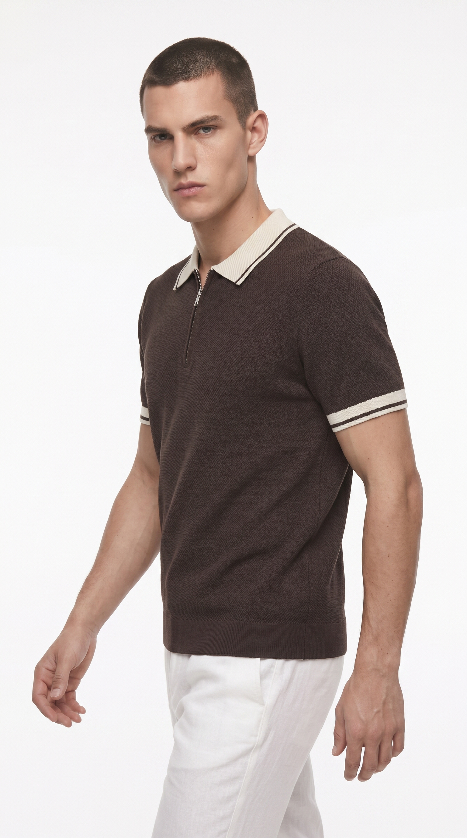 A man wearing a dark brown short-sleeve polo shirt with a cream collar and sleeve stripes, paired with white trousers, photographed against a plain white studio background, from Meleche Fashion USA or Meléche (short as (Mé))