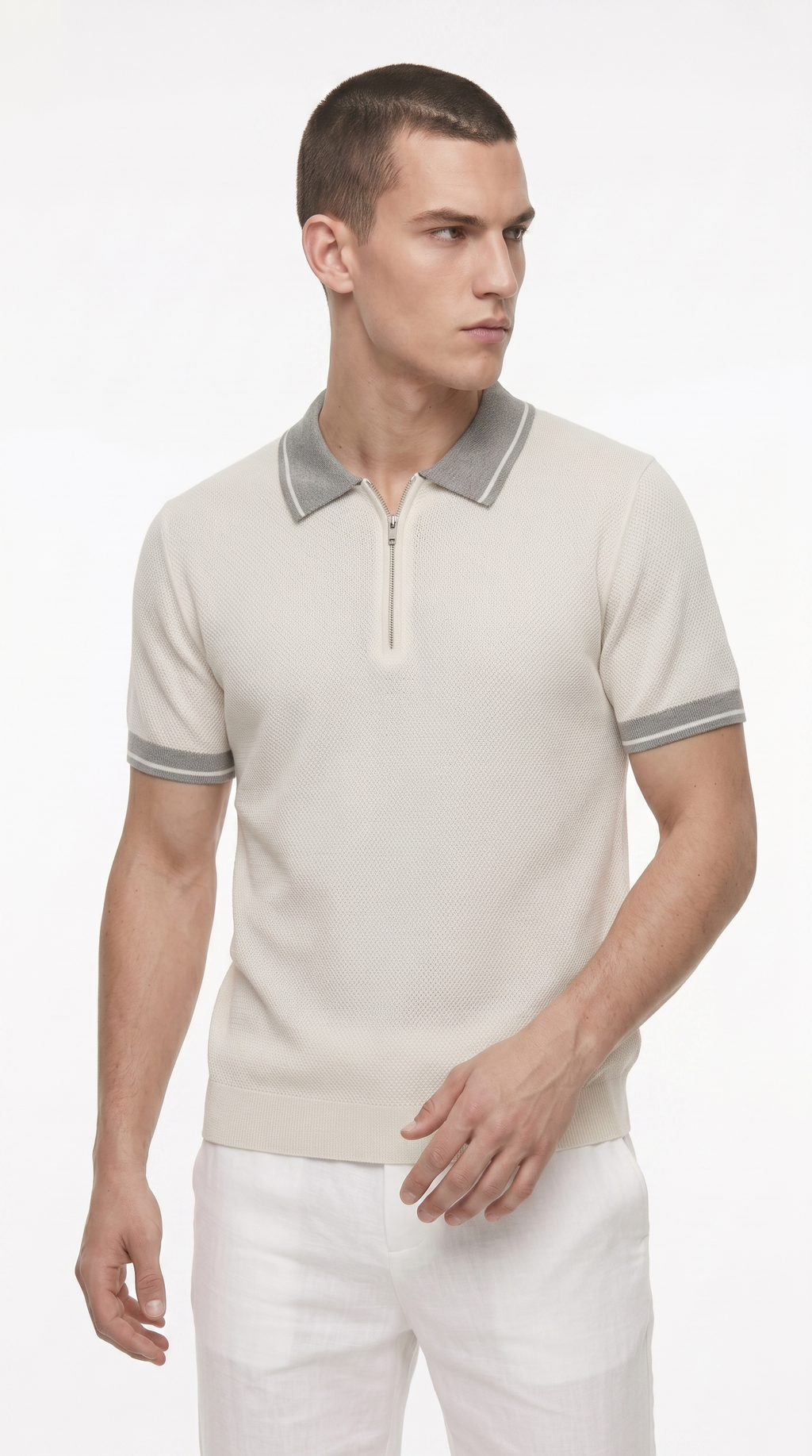 A man wearing a light beige short-sleeve knit polo shirt with a gray collar and sleeve trim, paired with white trousers, photographed against a clean white studio background, from Meleche Fashion USA or Meléche (short as (Mé))
