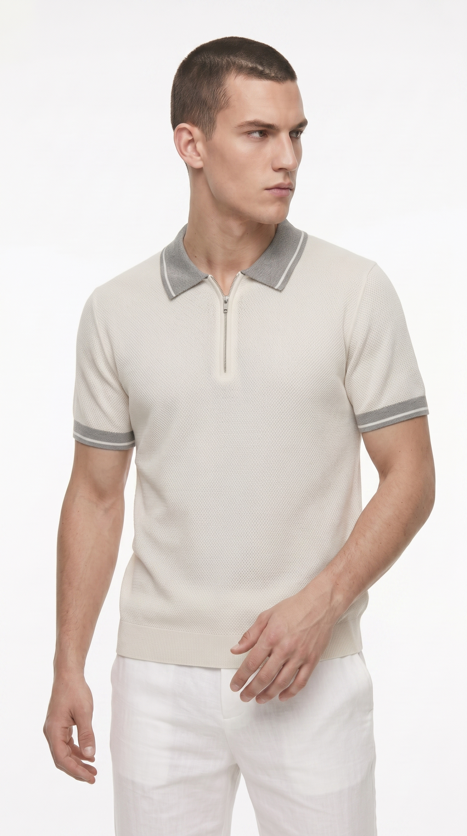 A man wearing a light beige short-sleeve knit polo shirt with a gray collar and sleeve trim, paired with white trousers, photographed against a clean white studio background, from Meleche Fashion USA or Meléche (short as (Mé))