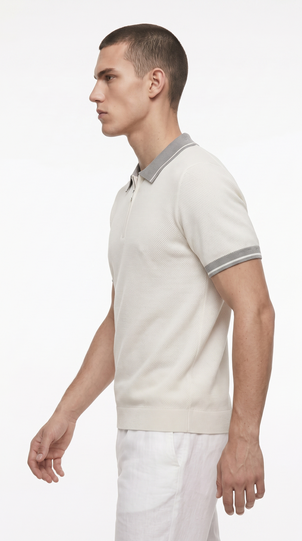 A man in profile wearing a light beige short-sleeve polo shirt with a contrasting gray collar and sleeve stripes, paired with white trousers, against a plain white studio background, from Meleche Fashion USA or Meléche (short as (Mé))
