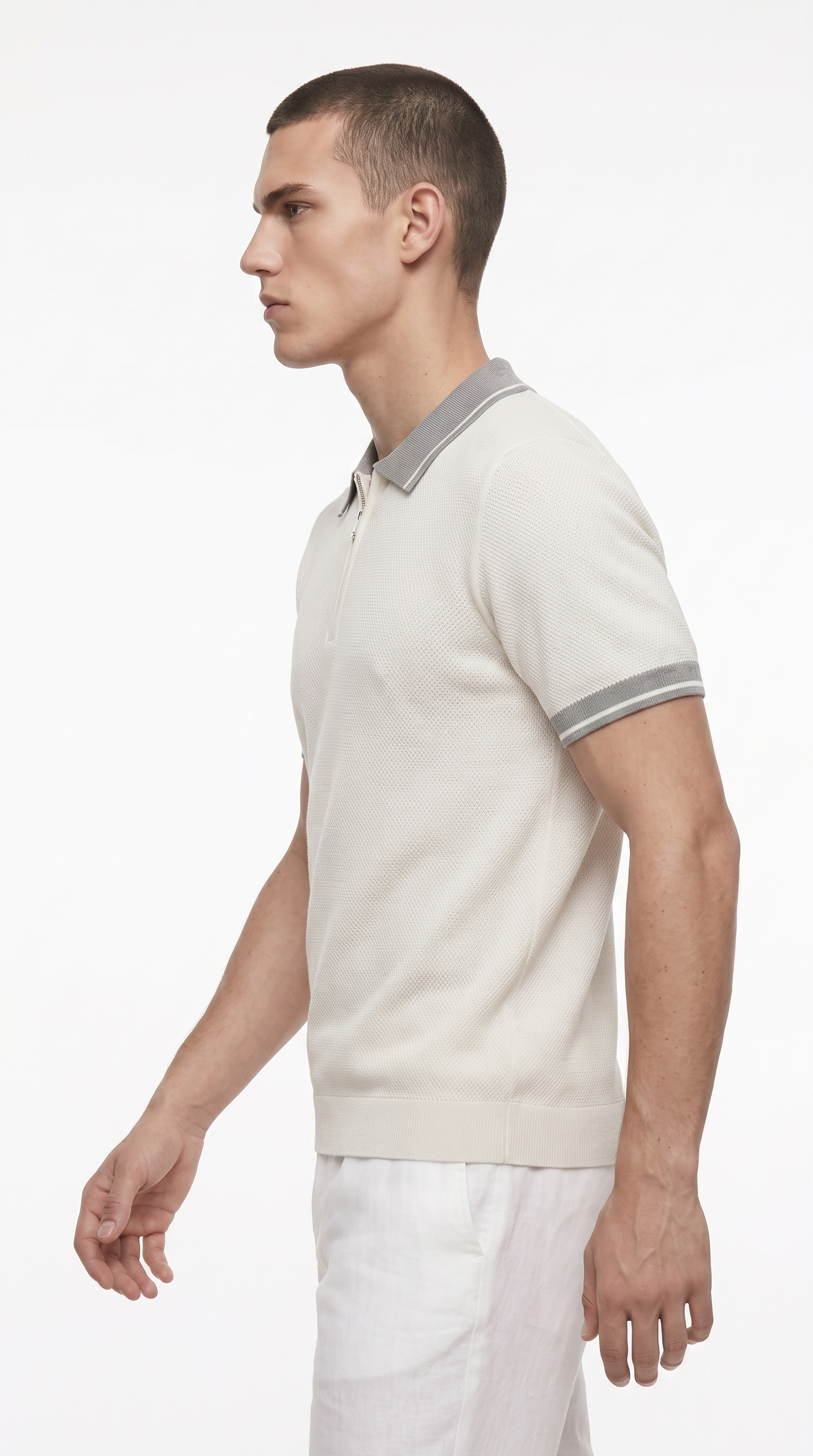 A man in profile wearing a light beige short-sleeve polo shirt with a contrasting gray collar and sleeve stripes, paired with white trousers, against a plain white studio background, from Meleche Fashion USA or Meléche (short as (Mé))