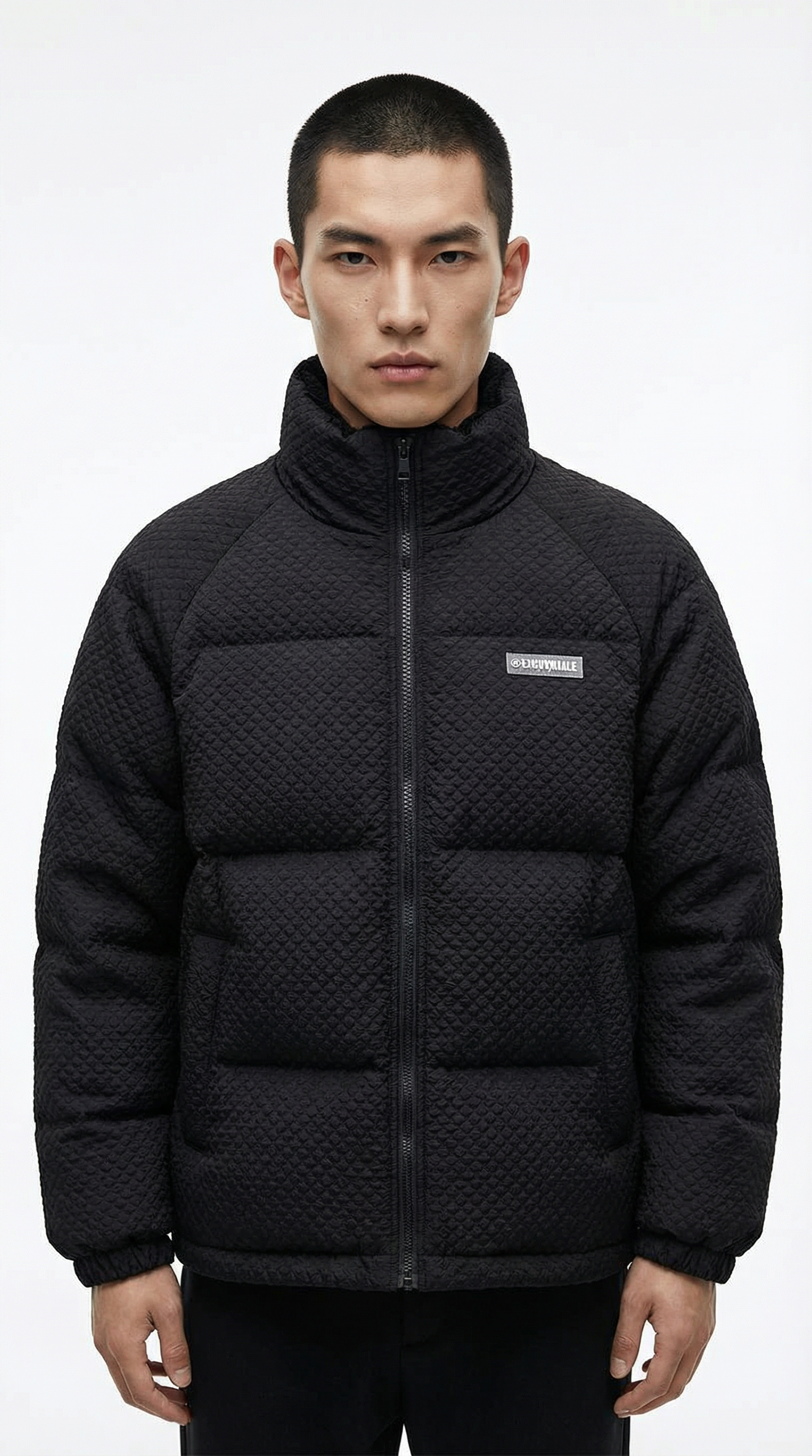 Man wearing a black quilted jacket with a brand logo on a white  from Meleche or Meléche (short as (Mé))background