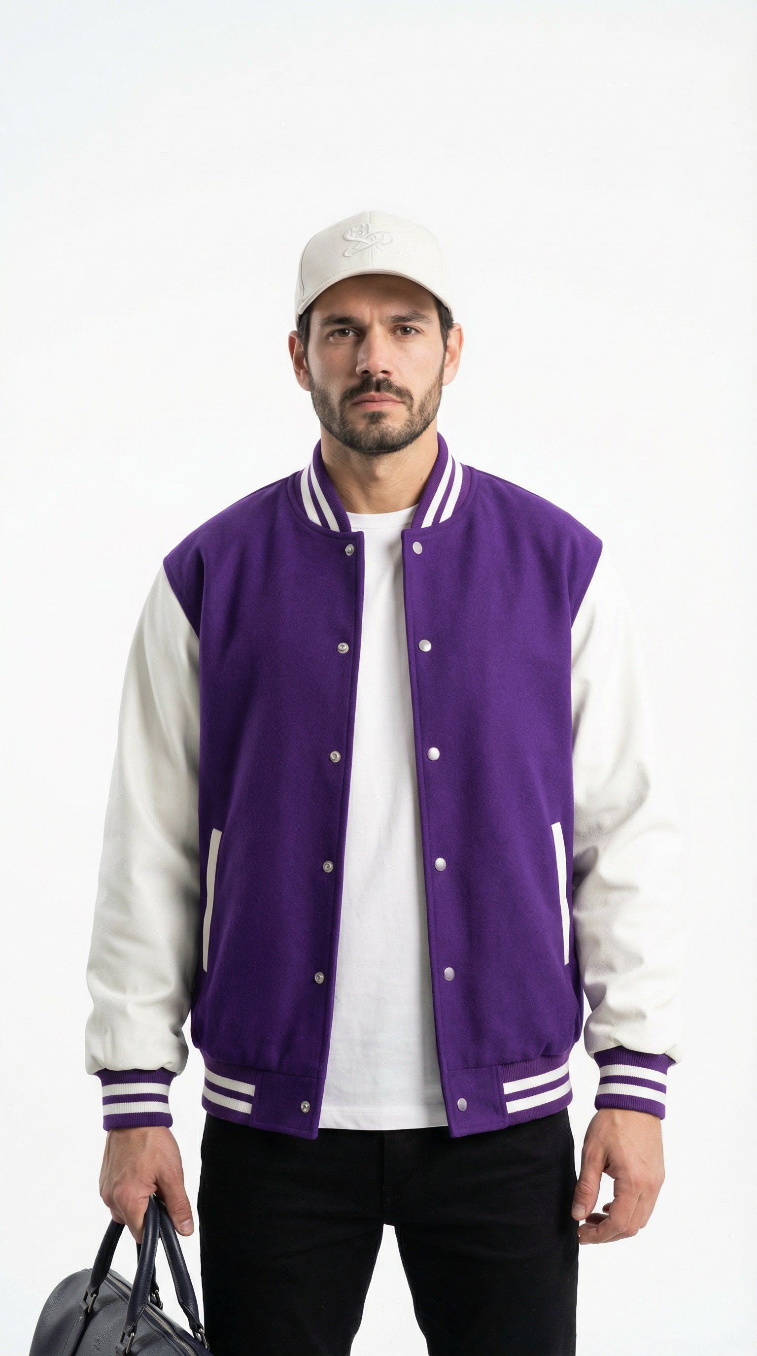 Man wearing a purple and white varsity jacket holding a black jacket against a gray wall.