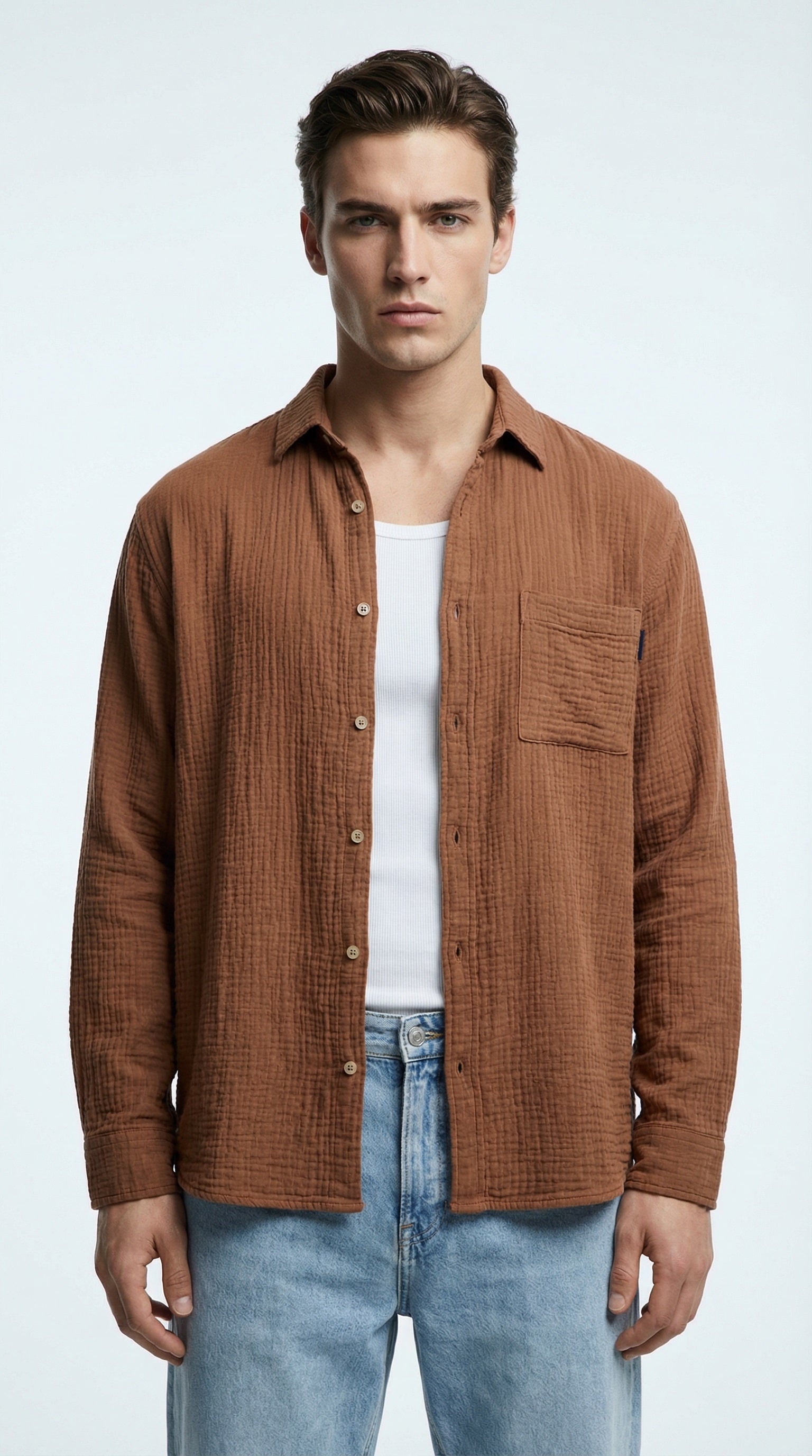 Man wearing a brown shirt and jeans standing outdoors.