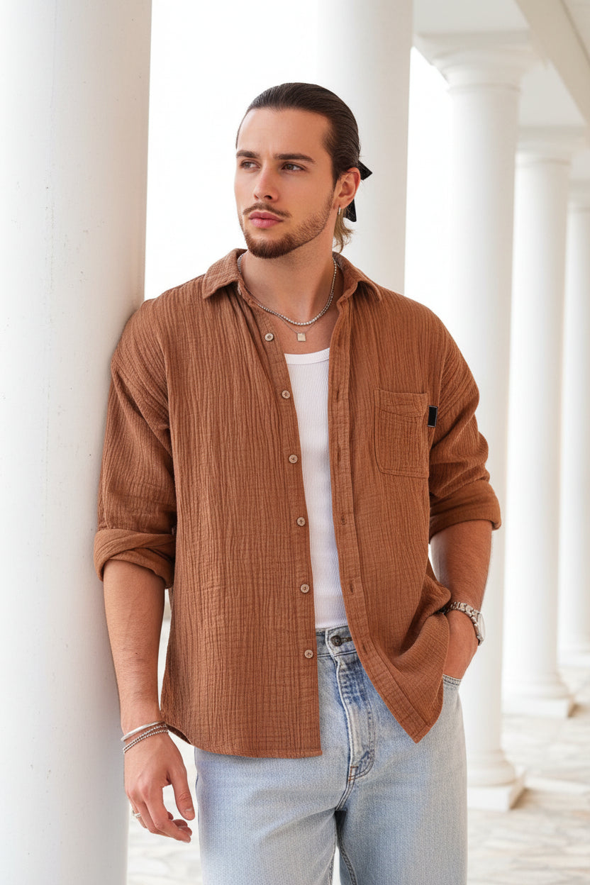 Man wearing a brown button-up shirt over a white tank top, standing outdoors.