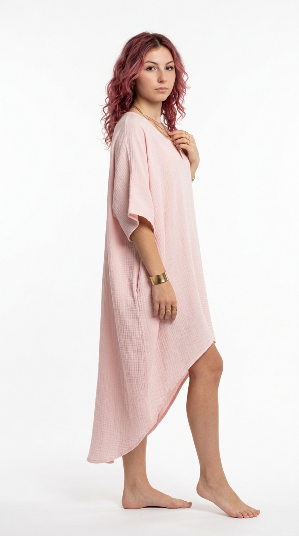 A woman modeling a light pink textured kaftan dress with a high-low hem, standing against a plain white studio background, from Meleche Fashion or Meléche (short as (Mé)) and shoot taken by Meléche studio photography NYC-USA