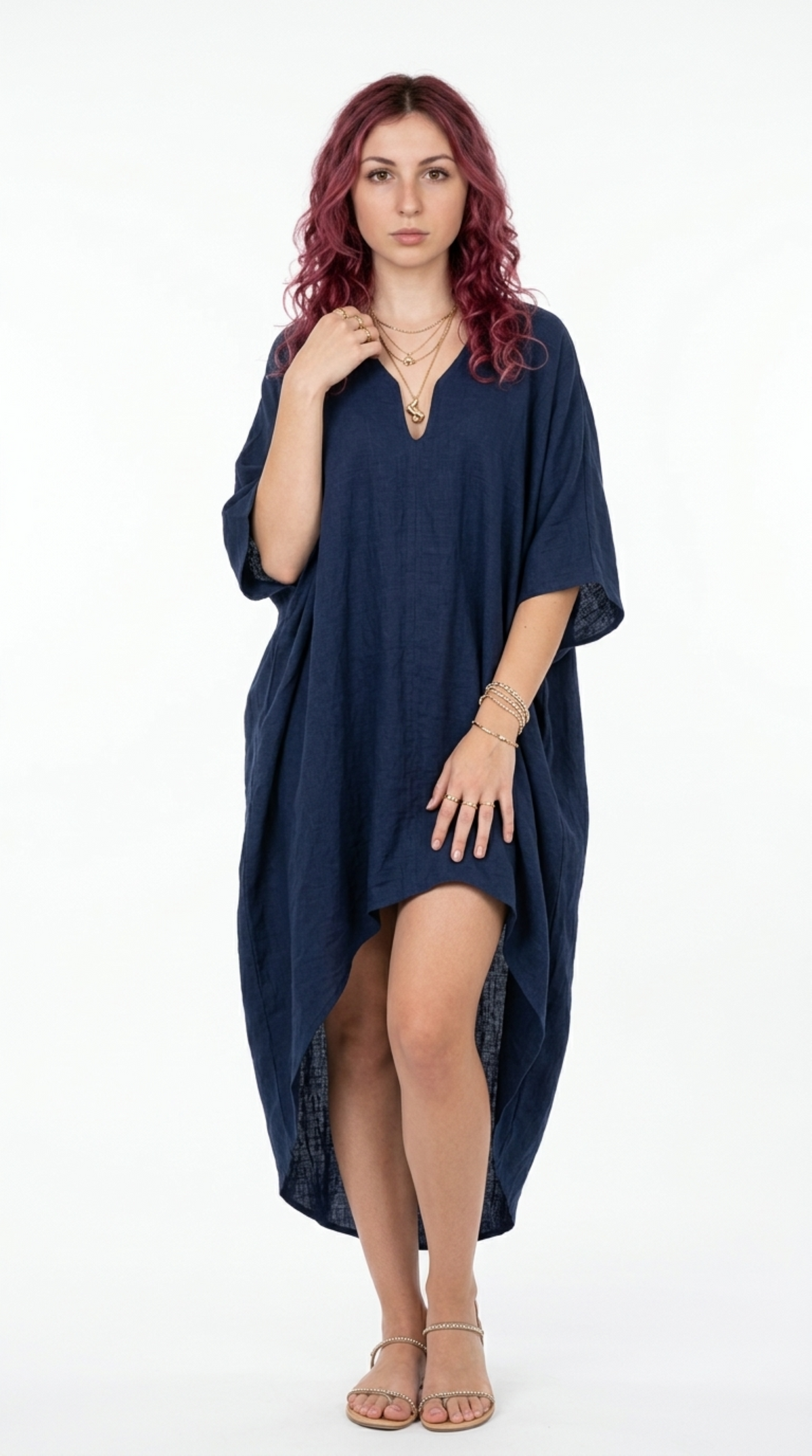 A woman with wavy red hair wearing a loose, dark navy blue kaftan-style dress with a split high-low hem, standing against a plain white studio background, from Meleche Fashion or Meléche (short as (Mé)) and shoot taken by Meléche studio photography NYC-USA