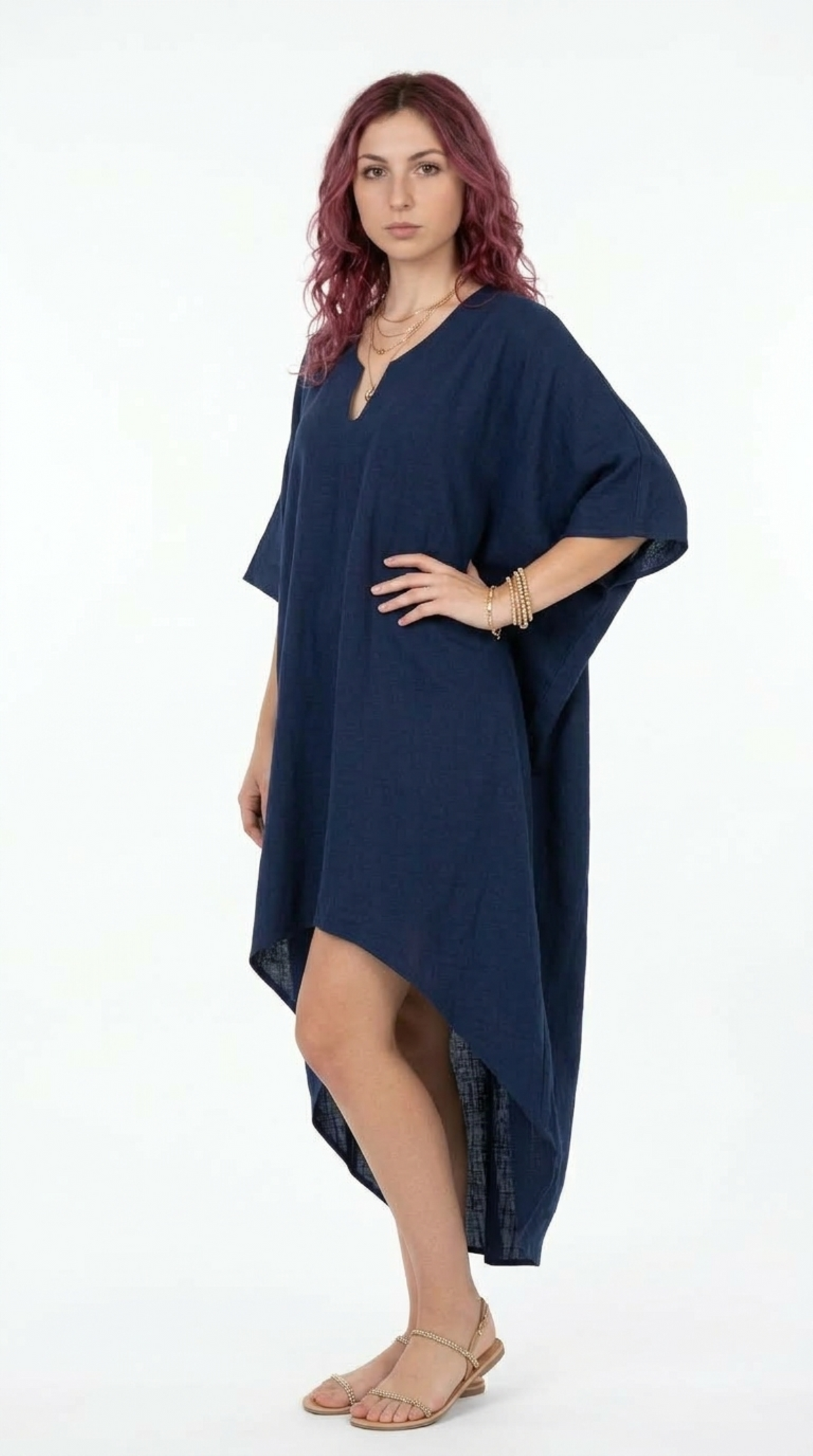 A woman modeling a loose, high-low navy blue kaftan dress with wide short sleeves and a V-neckline, paired with gold jewelry and flat sandals against a white studio background, from Meleche Fashion or Meléche (short as (Mé)) and shoot taken by Meléche studio photography NYC-USA
