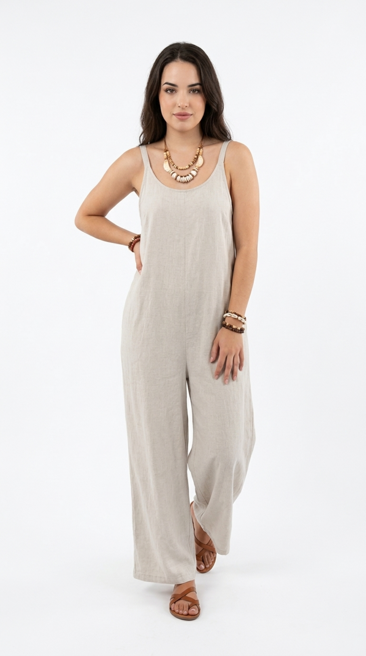 A woman modeling a light beige linen wide-leg jumpsuit with a scoop neck, paired with brown leather sandals and gold jewelry, against a plain white studio background, from Meleche Fashion or Meléche (short as (Mé)) and shoot taken by Meléche studio photography NYC-USA
