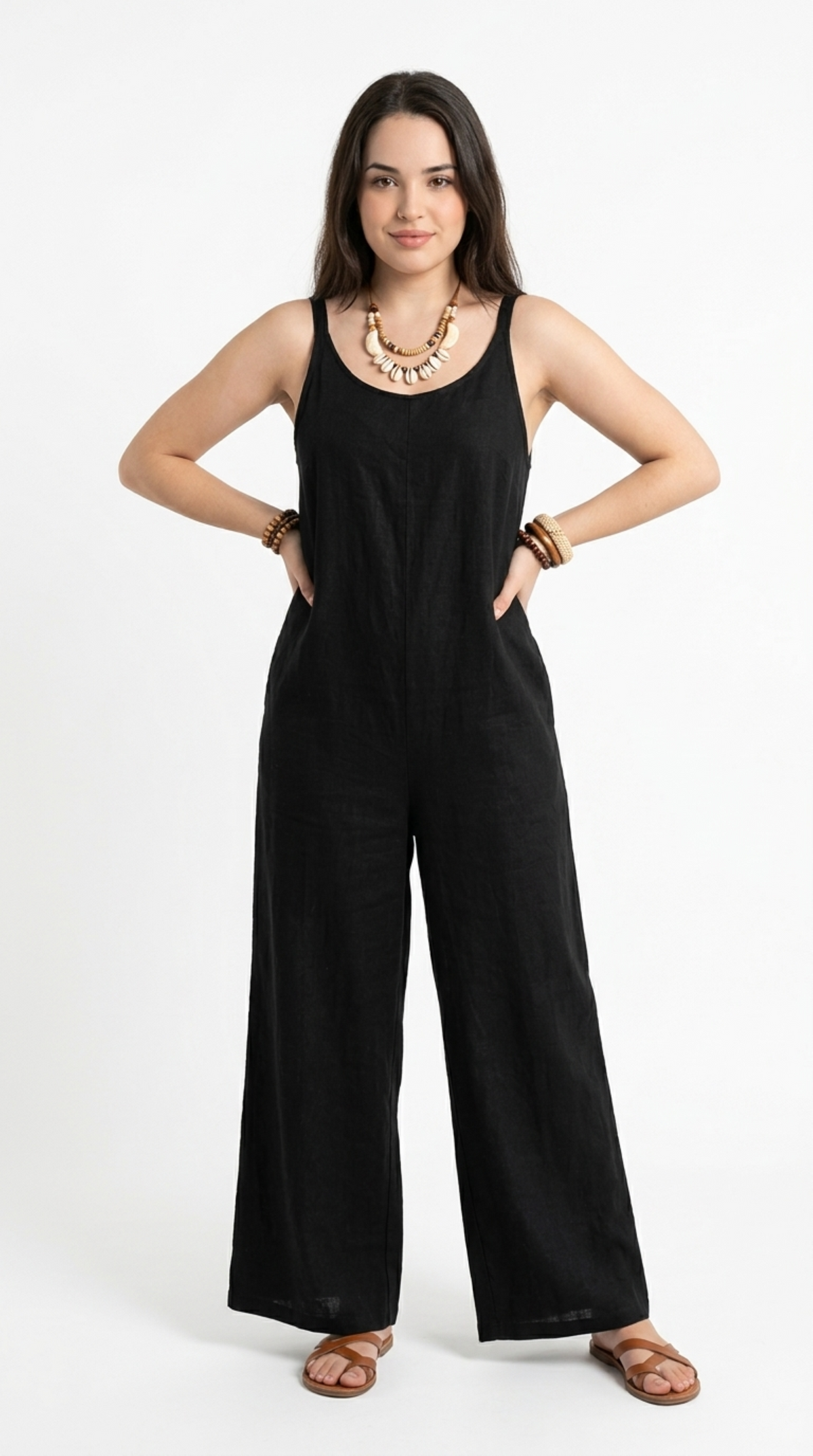 A woman modeling a black wide-leg sleeveless jumpsuit with a textured linen-like fabric, styled with a chunky gold necklace and brown leather sandals against a plain white studio background, from Meleche Fashion or Meléche (short as (Mé)) and shoot taken by Meléche studio photography NYC-USA