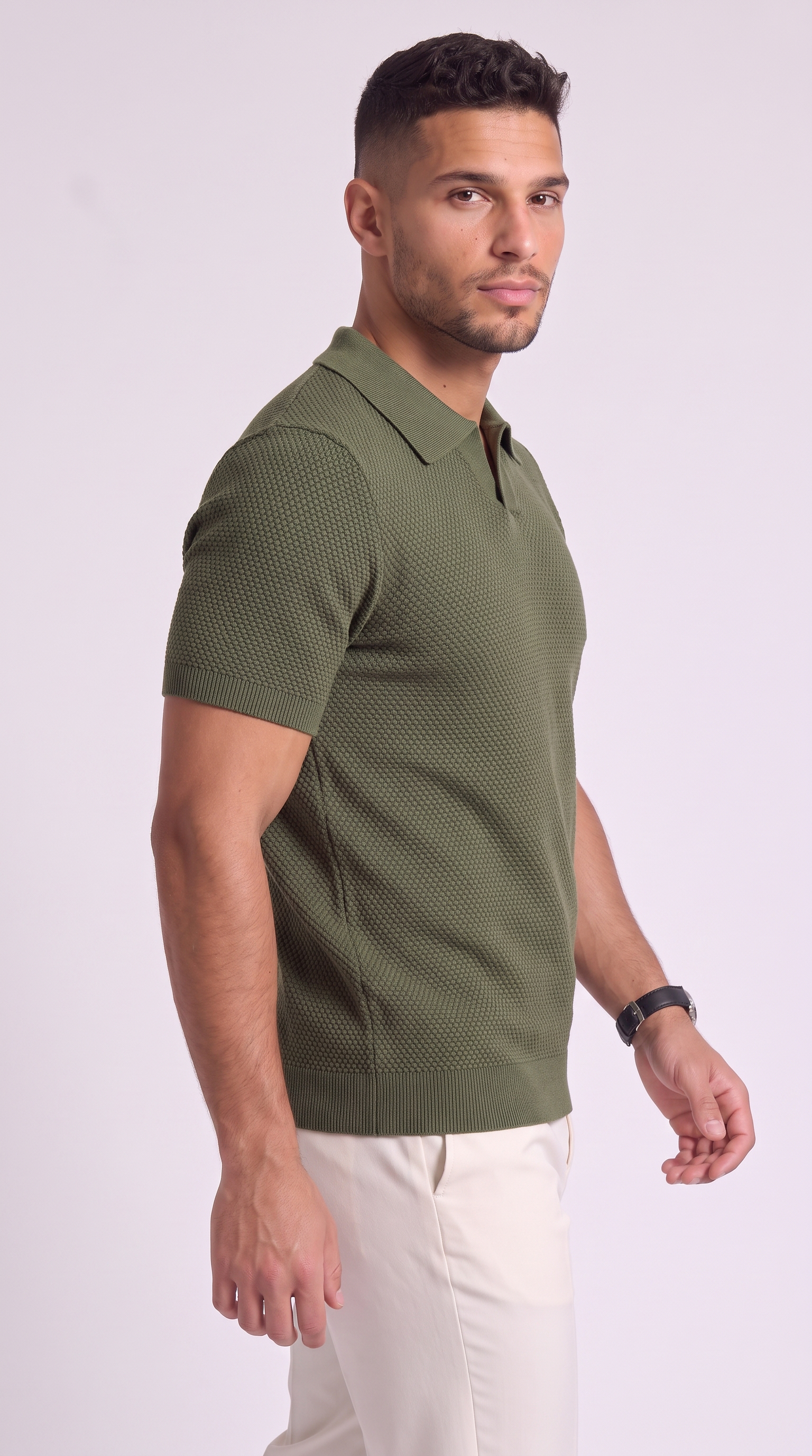 A man wearing a textured olive green short-sleeve polo shirt and off-white trousers, standing against a light gray studio background, from Meleche Fashion USA or Meléche (short as (Mé))