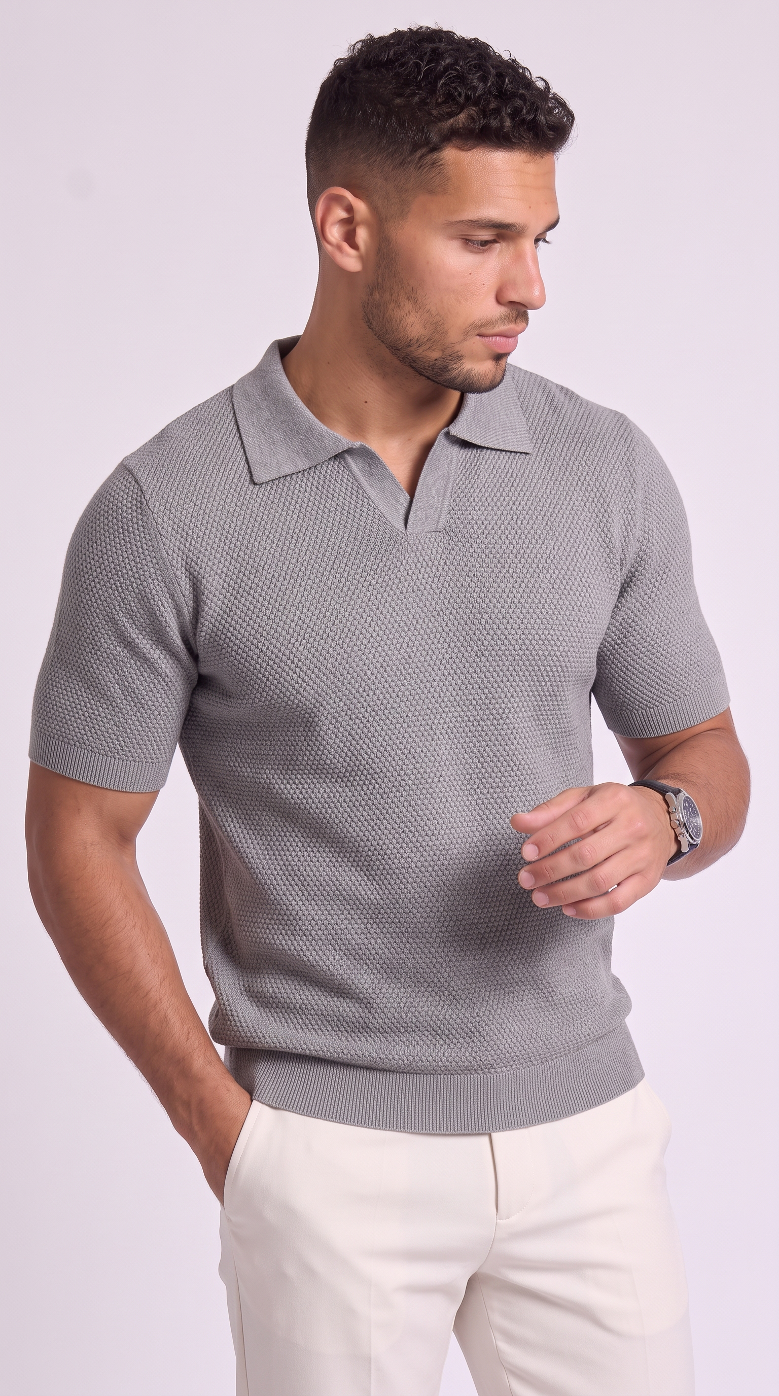 A man wearing a gray short-sleeve polo shirt with a textured knit pattern and white trousers, standing against a light gray studio background, from Meleche Fashion USA or Meléche (short as (Mé))