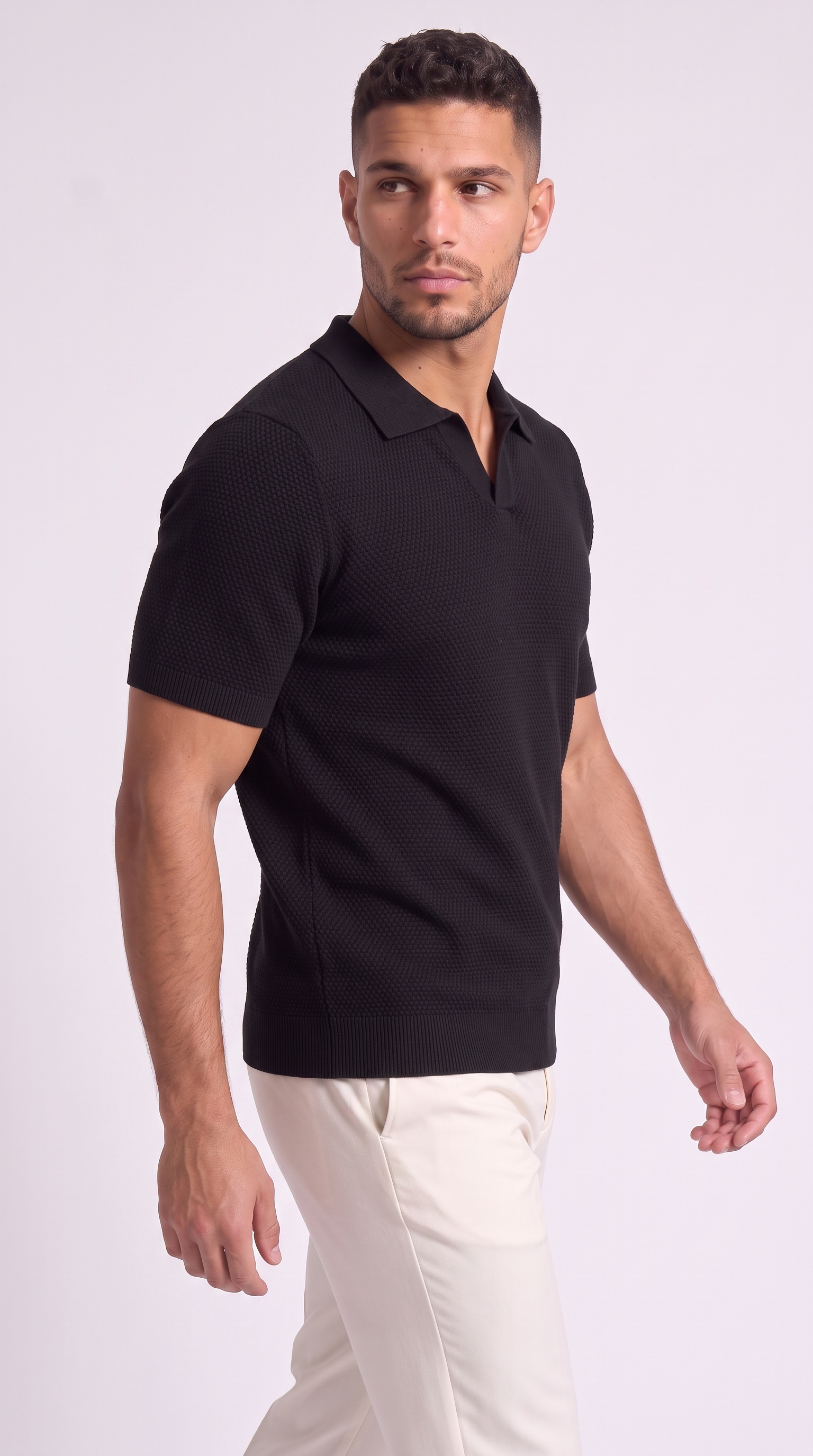 A man wearing a black short-sleeve polo shirt with a textured knit pattern and white trousers, photographed against a light gray studio background, from Meleche Fashion USA or Meléche (short as (Mé))