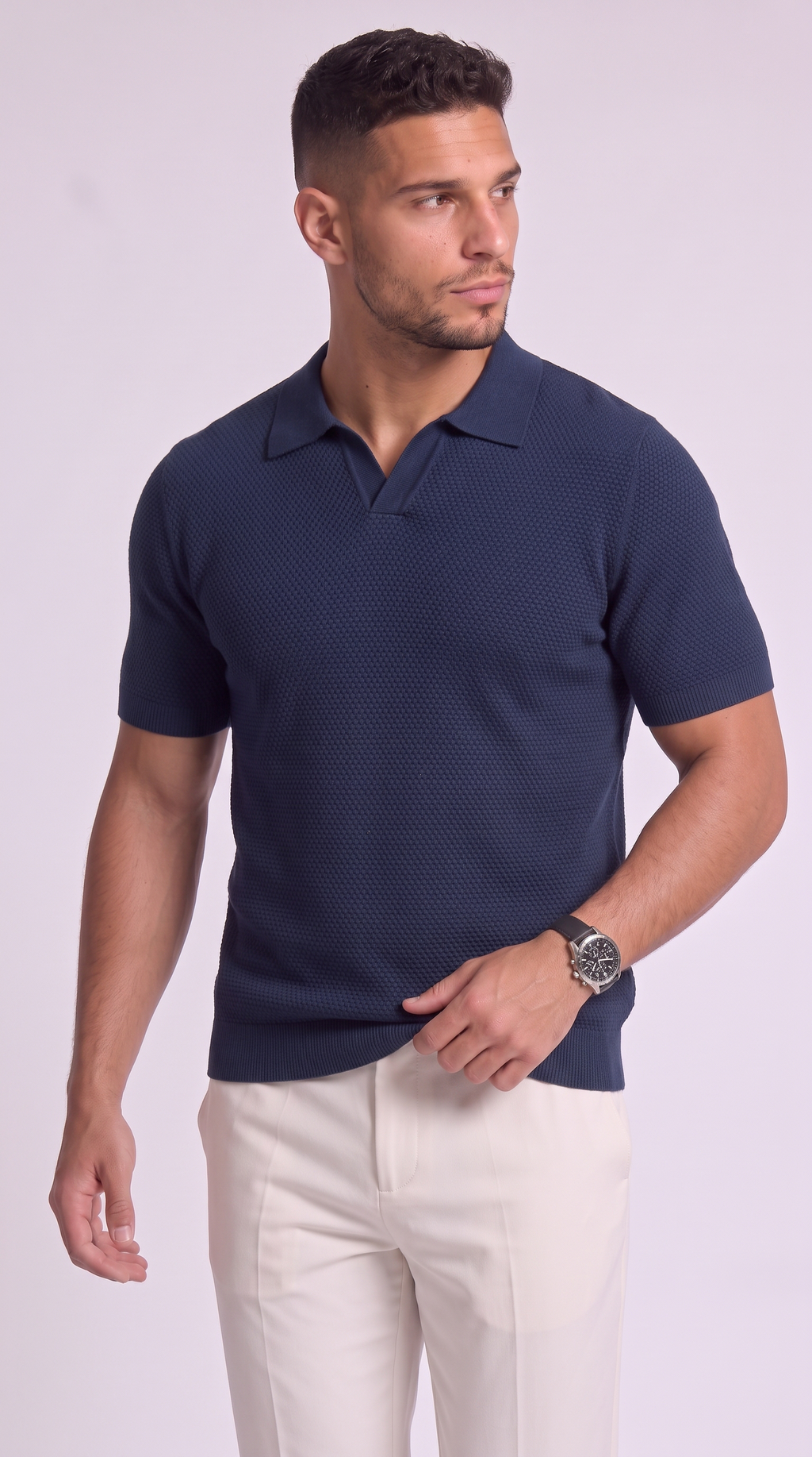 A man wearing a dark navy blue short-sleeve polo shirt with a subtle textured pattern, paired with off-white trousers, standing against a light lavender studio background, from Meleche Fashion USA or Meléche (short as (Mé))