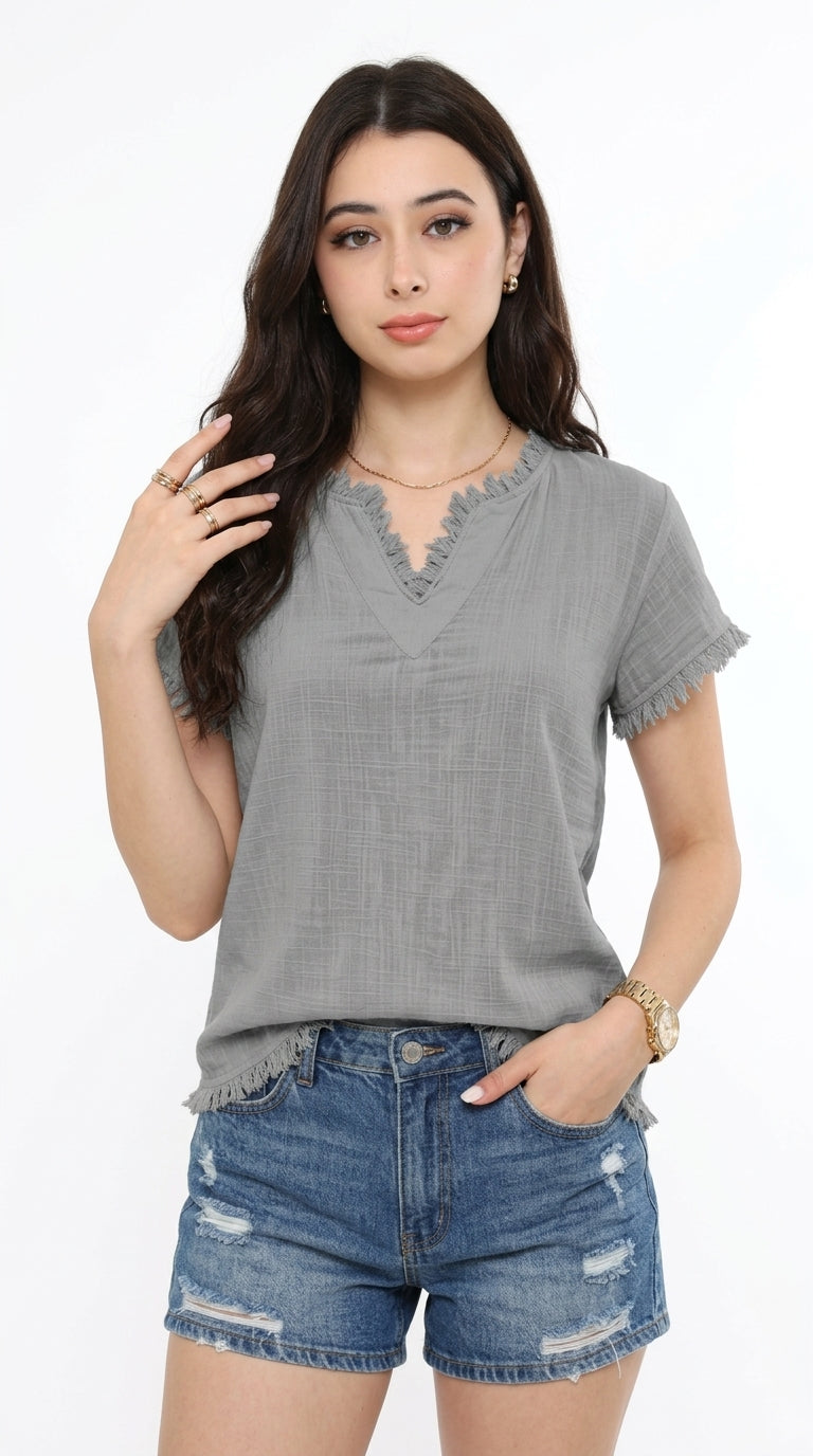 A woman modeling a gray short-sleeve V-neck top with ruffled trim and frayed edges, paired with distressed denim shorts, against a plain white background, from Meleche Fashion USA or Meléche (short as (Mé))