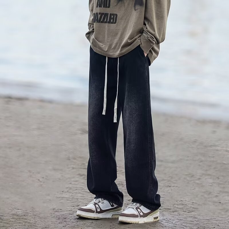 Person wearing black pants and a beige sweatshirt on a beach.