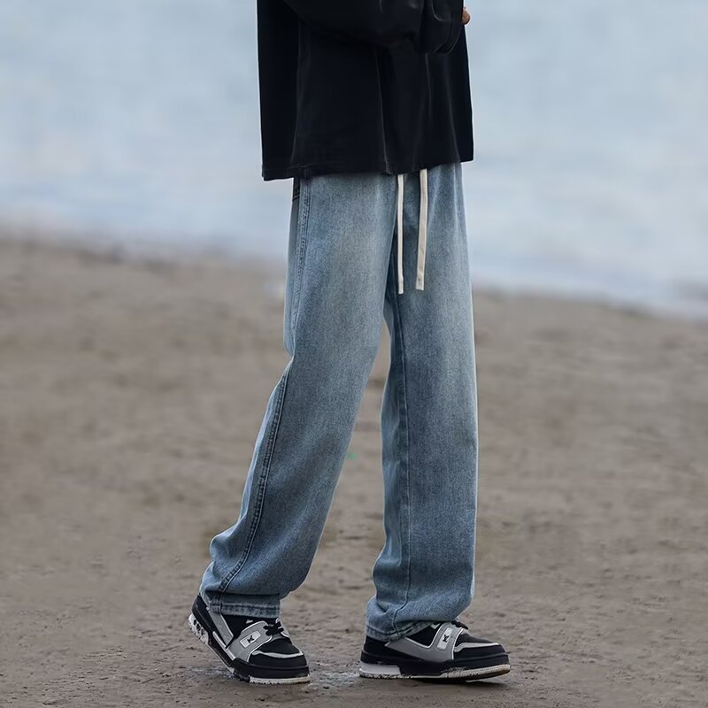 Person wearing blue jeans and black shoes on a beach