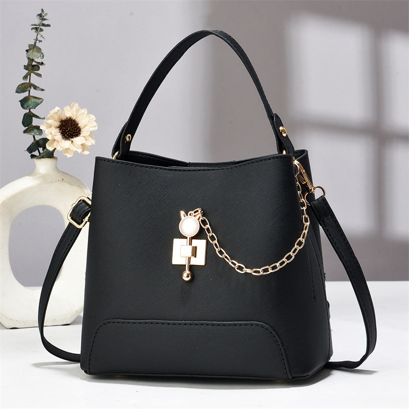 Xen - Black handbag with gold chain detail on a white surface with a blurred background