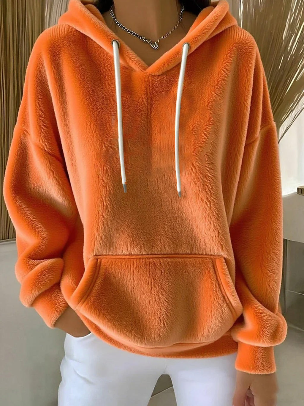 Orange fleece hoodie with white drawstrings worn by a person indoors.
