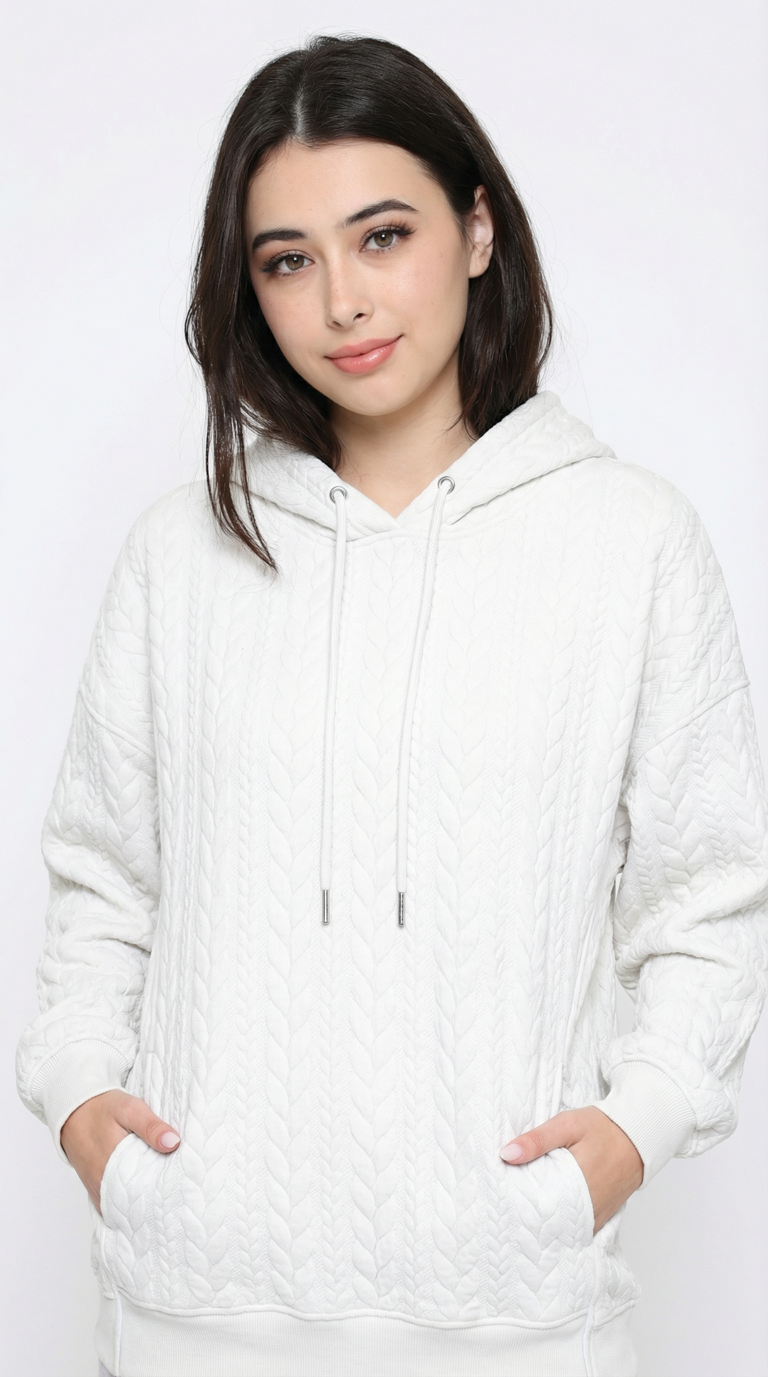 Woman wearing a white cable knit hoodie against a plain background