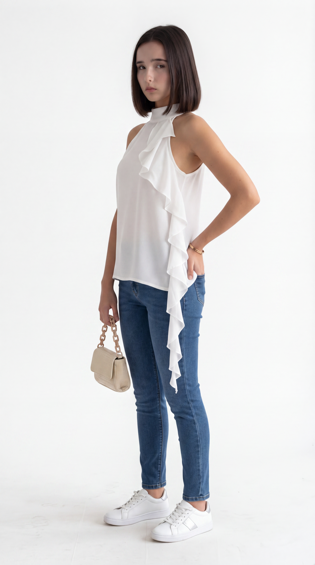 A woman modeling a white sleeveless ruffled top, blue skinny jeans, and white sneakers, holding a small beige handbag against a plain white studio background, from Meleche Fashion USA or Meléche (short as (Mé))