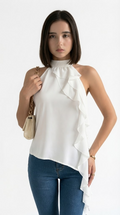 A woman modeling a white halter-neck blouse with cascading ruffles and an asymmetrical hem, paired with blue jeans and a small beige shoulder bag against a plain white background, from Meleche Fashion USA or Meléche (short as (Mé))