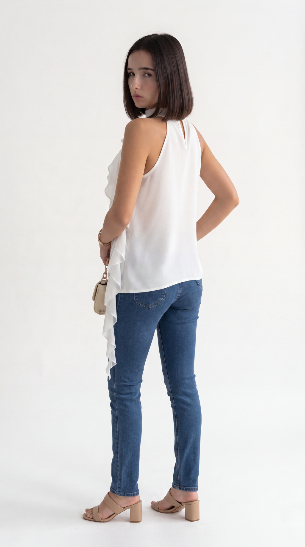 A woman wearing a white sleeveless ruffled top, blue skinny jeans, and beige block-heel sandals, photographed from the back against a plain white studio background, from Meleche Fashion USA or Meléche (short as (Mé))