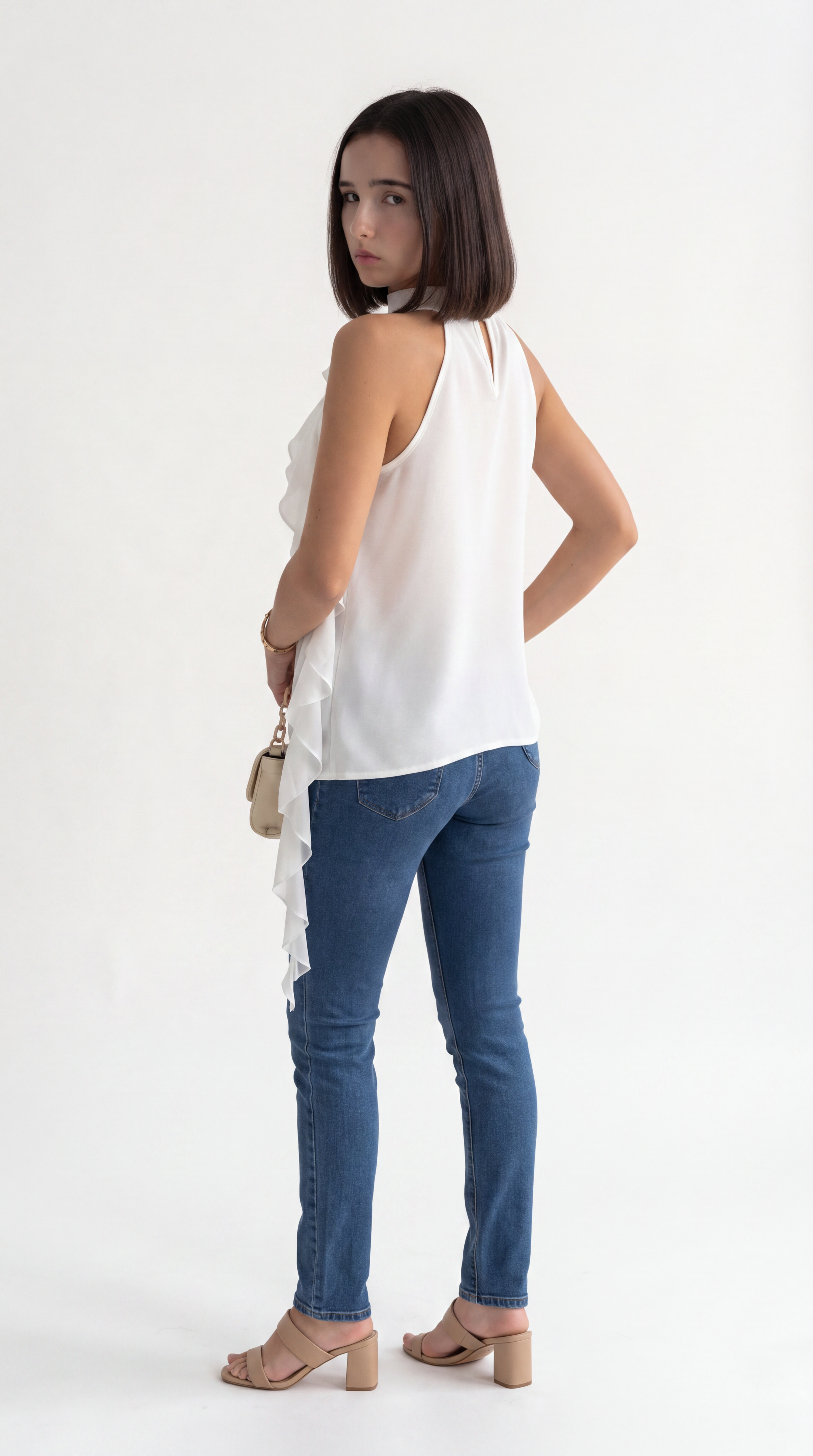 A woman wearing a white sleeveless ruffled top, blue skinny jeans, and beige block-heel sandals, photographed from the back against a plain white studio background, from Meleche Fashion USA or Meléche (short as (Mé))